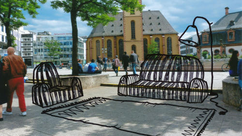 Auf einem Foto, das den Platz an der Frankfurter Hauptwache bei sommerlichem Wetter zeigt, sind mit schwarzem Stift Teppich, Sofa, Sessel und Stehlampe dazu gemalt.